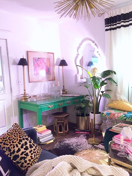 a bold maximalist home office with lilac walls, an emerald desk, a black sofa and lots of colorful textiles, gilded touches