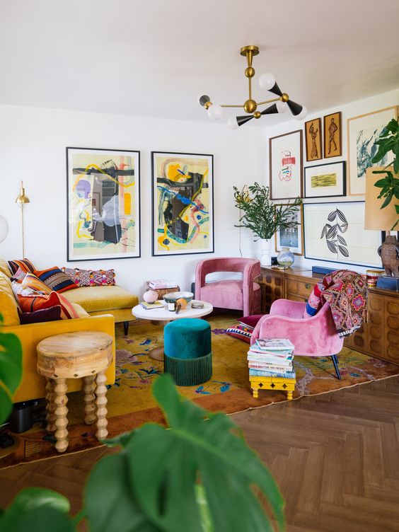 a bold maximalist living room with a mustard sectional, pink chairs, an emerald pouf, a bold gallery wall and a bright rug plus statement plants