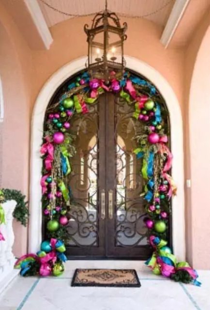 a bright Christmas inspired entrance with colorful oversized ornaments and ribbons framing the doors make the space very holiday like