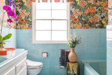 a bright maximalist bathroom with blue tiles and a bathtub, bright florla wallpaper, bold blooms and a sunbrust chandelier