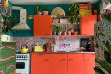 a bright maximalist kitchen with coral furniture, a bright floor and rug, a green wall and a colorful backsplash plus lots of potted plants
