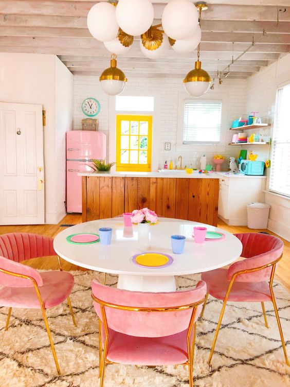 a candy colored maximalist kitchen with a neon yellow window, a pink fridge, pink velvet chairs and pastel tableware