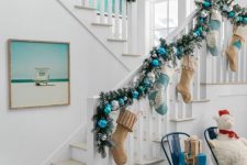 a charming coastal space with an evergreen blue and silver ornament garland, neutral and blue stockings, navy chairs and coastal photos is amazing