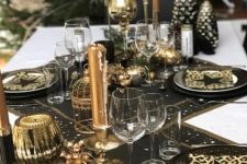 a chic black and gold party tablescape with black table runners and placemats, black and gold plates, gold candles and candleholders