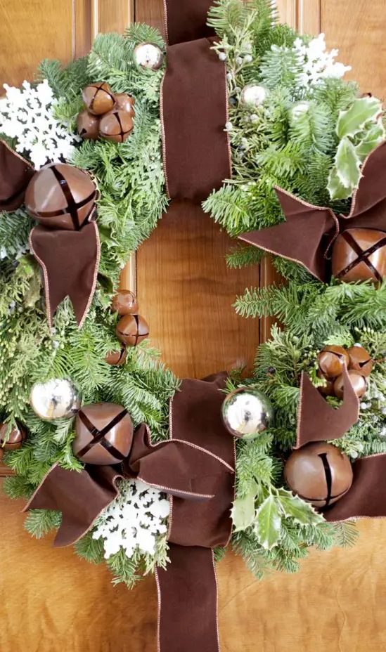 a chic fir wreath with bells, silver ornaments, white snowflakes and oversized brown bells and brown ribbon is a lovely and chic idea for the holidays