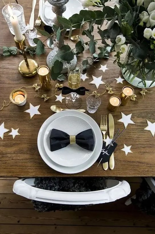 a chic table setting with white and gold stars, white blooms, eucalyptus, gold cutlery and candle holders