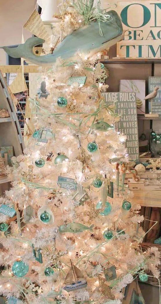 a coastal chic Christmas tree in white, with aqua and mint ornaments, branches, signs, boats and a large whale as a tree topper