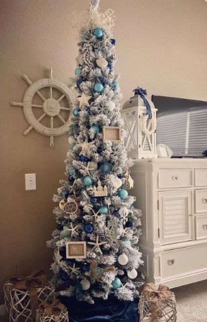a coastal flocked Christmas tree with white, turquoise and navy ornaments, starfish, turtles, frames and corals on top is wow