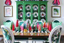 a colorful Christmas dining room with a green buffet with colorful ornaments in mugs, colorful bottle brush Christmas trees on the table and pink bows
