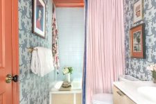 a colorful maximalist bathroom with grey printed walls, a rust ceiling and a door, a bold rug, a creative agate chandelier and a pink curtain
