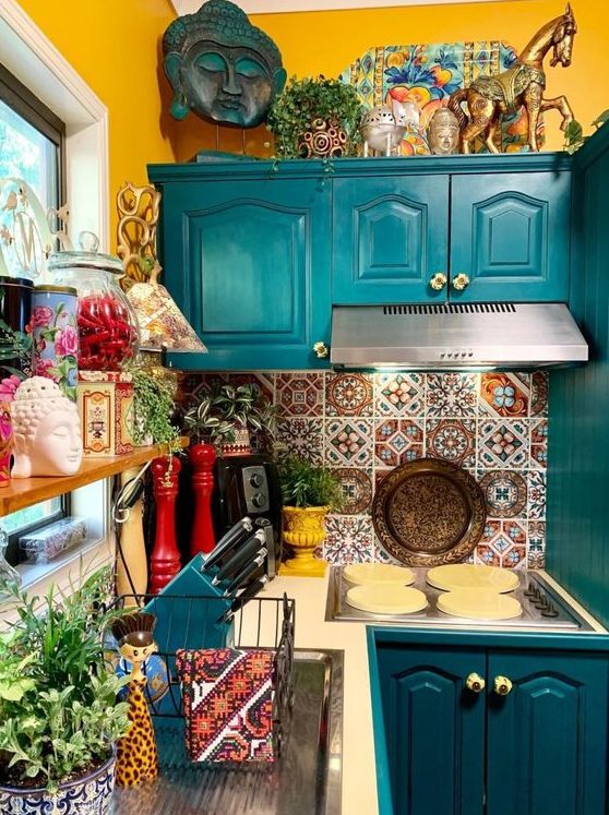 a colorful maximalist kitchen with mustard walls, teal cabinets, colorful tiles on the backsplash and lots of accessories and potted plants