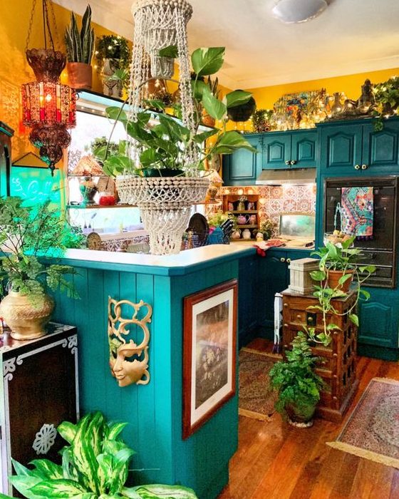 a colorful maximalist kitchen with yellow walls, emerald cabinets, a colorful tile backsplash and lots of potted plants