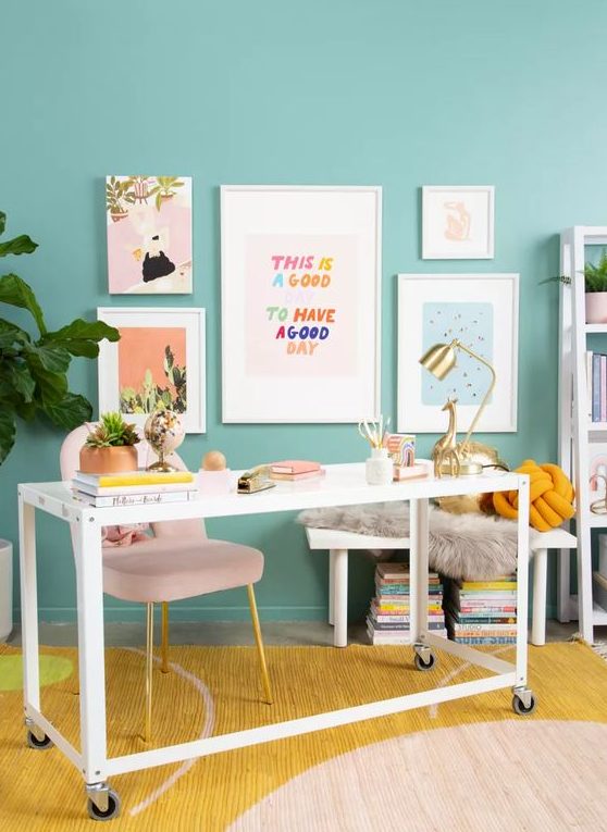 a colorful working space with turquoise walls, a blush chair, a white desk, a colorful rug and a bright gallery wall