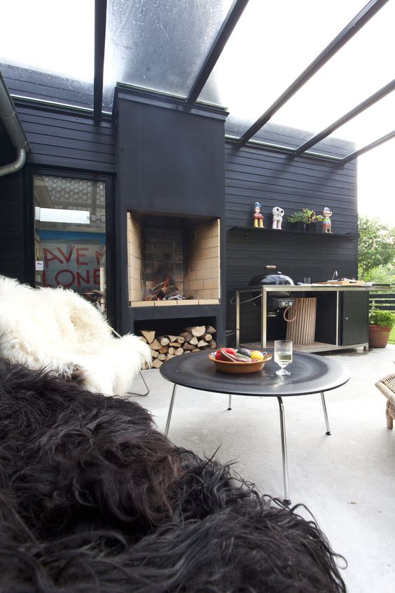 a contemporary winter terrace with a sheer roof, a fireplace with firewood, a grill table, a large coffee table and faux fur chairs around it
