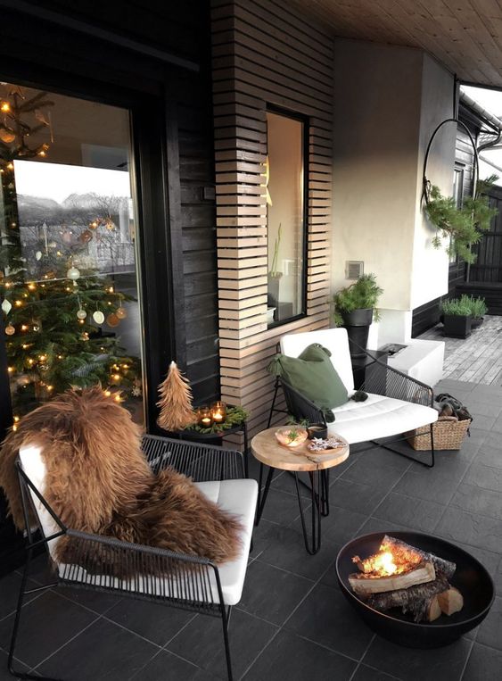 a contemporary winter terrace with black metal furniture, a hairpin leg table, a fire bowl and faux fur plus candles and a small tree