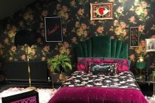 a dark maximalist bedroom with a dark floral accent wall, a dark green velvet bed, a feather chandelier, bold floral and purple bedding and a neon light