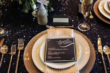 a dark sequin tablecloth, gold glitter chargers, gold cutlery and a lush greenery and bloom centerpiece
