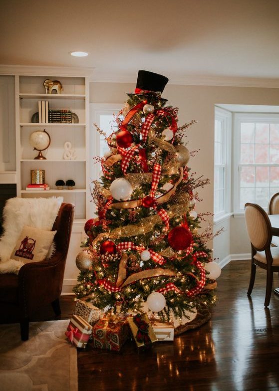 a decorated Christmas tree with lights, burlap and plaid ribbons, oversized red, gold and white ornaments and a hat on top