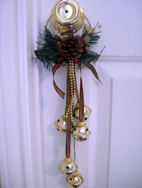a door accent with bells on striped ribbons, fir branches, a pinecone and a striped bow is bold, glam and colorful