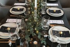 a dreamy tablescape in black, with black linens, white porcelain, a greenery runner with LED lights, tall and thin candles