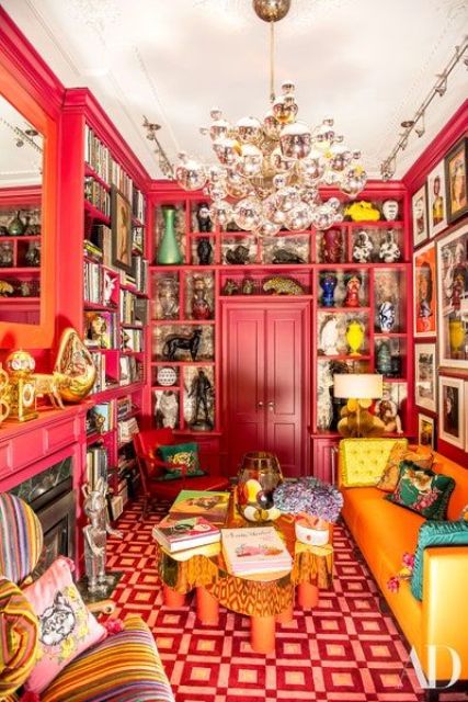 a fantastic maximalist living room with pink walls and built in shelves, a bold printed rug, an orange sofa, a built in fireplace and a crystal chandelier