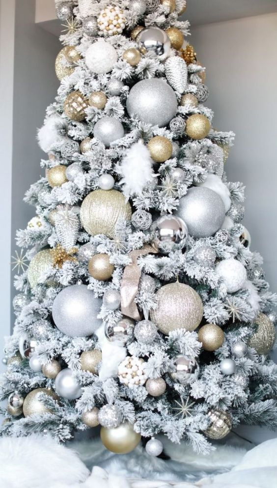 a flocked Christmas tree wiht oversized and regular-shaped silver and gold ornaments including glitter ones is a chic and glam solution