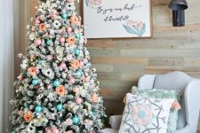 a flocked Christmas tree with blue and ornaments, peachy and white blooms, twigs is a creative and cool idea to rock