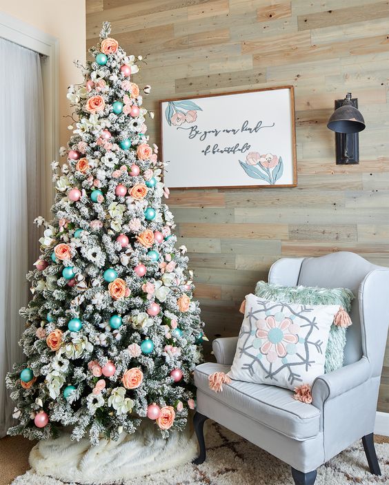 a flocked Christmas tree with blue and ornaments, peachy and white blooms, twigs is a creative and cool idea to rock