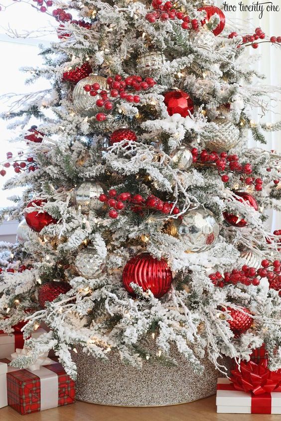 a flocked Christmas tree with oversized red berries, lights, silver and metallic ornaments and oversized red ones is amazing