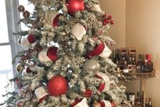 a flocked Christmas tree with oversized red, silver glitter ornaments and red and white ribbons plus smaller ornaments and berries