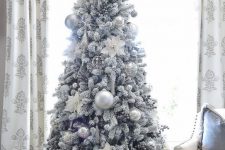 a flocked Christmas tree with silver and silver glitter usual and oversized Christmas ornaments looks frozen