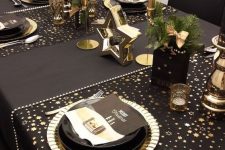 a glam black and gold party table with star printed placemats, black plates and gold chargers, gold candles and stars