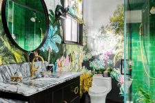 a gorgeous maximalist bathroom with botanical motifs, with printed tiles, green ones in the shower, bold floral wallpaper and a black vanity