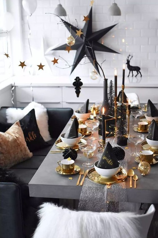 a gorgeous silver, gold and black Christmas tablescape with gold chargers, cutlery, mugs, candleholders and black candles plus an oversized black paper star