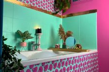 a jaw-dropping bathroom ith a hot pink wall and bold printed panels, bold green tiles, touches of gold and some potted plants