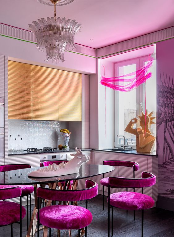 a jaw dropping maximalist kitchen with white and gold ribbed cabinets, a white tile backsplash, hot pink chairs and crazy sculptures