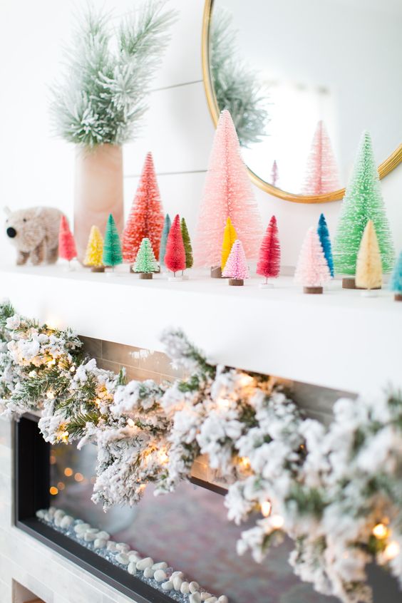 a mantel with colorful bottle brush Christmas trees and a flocked evergreen garland with lights for Christmas