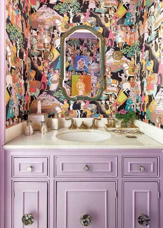 a maximalist bathroom with crazily printed wallpaper, a lilac built-in vanity and a mirror in a vintage frame is chic