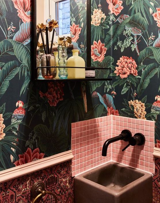 a maximalist bathroom with dakr floral wallpaper, pink tiles, a pink sink, black fixtures and a black shelf