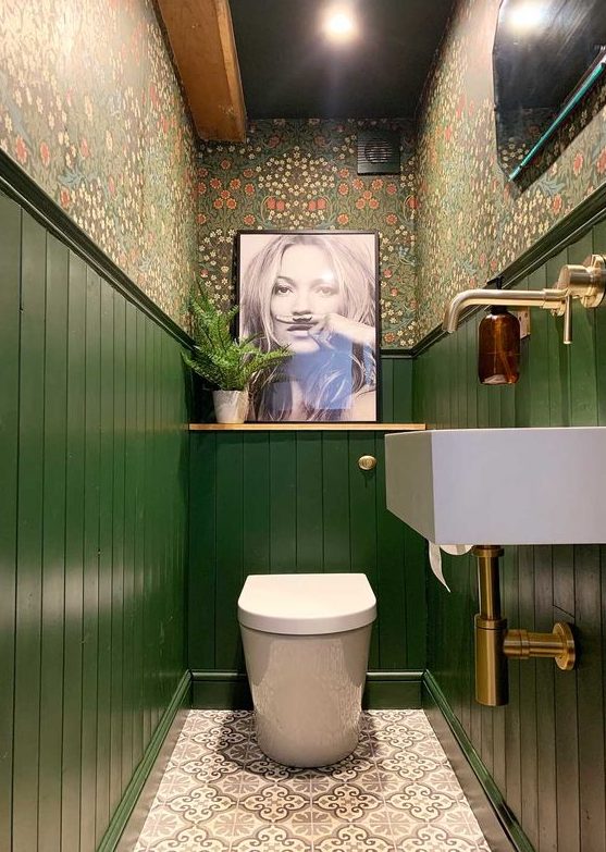 a maximalist bathroom with floral wallpaper, green paneling, an artwork and a statement artwork and brass touches