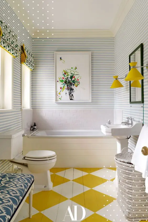 a maximalist bathroom with striped walls, a geo painted floor, an upholstered bench, some baskets, yellow lamps and printed curtains