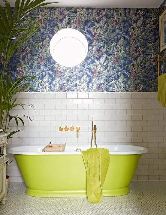 a maximalist bathroom with white subway tiles, dark tropical leaf wallpaper, a neon green bathtub and towels, a statement plant