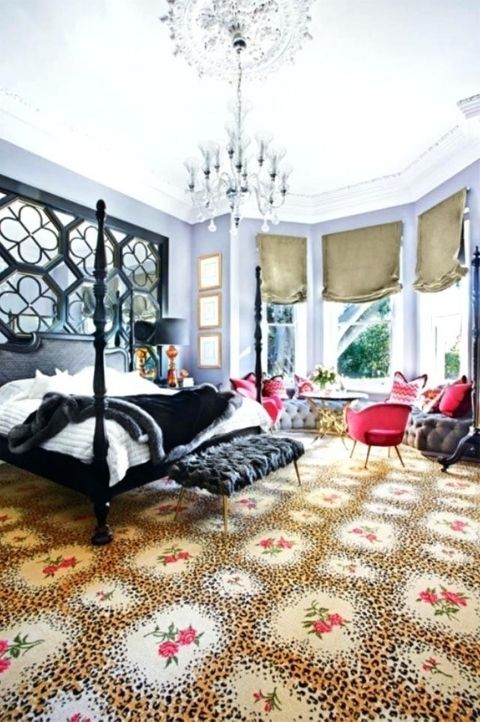 a maximalist bedroom with a bow window, a printed rug, a black bed with pillars and a matching mirror wall, a crystal chandelier