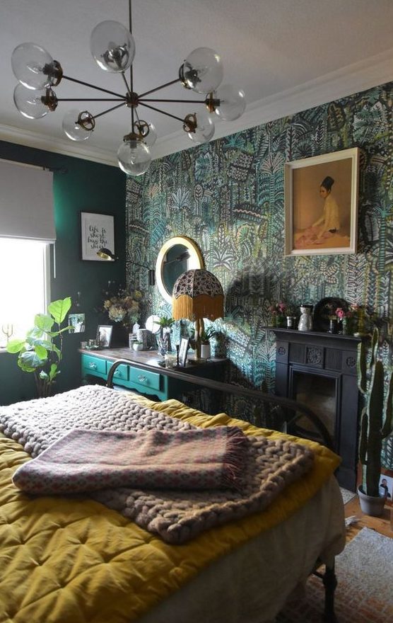 a maximalist bedroom with green walls and a botanical accent one, a black fireplace, a green console, a metal bed, bright bedding and a mirror