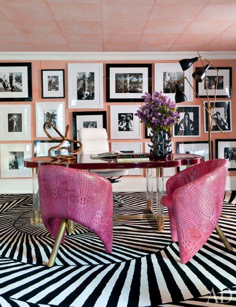 a maximalist home office with blush walls, a striped black and white rug, a black and white gallery wall, a red wood desk and pink leather chairs
