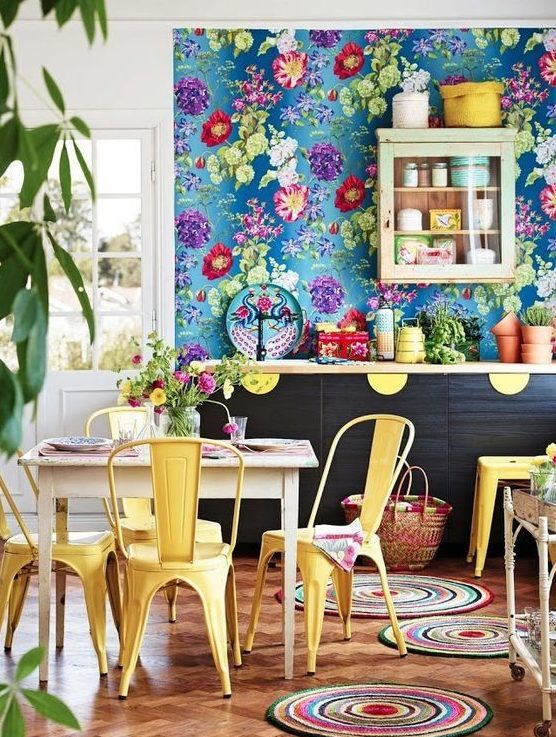 a maximalist kitchen with a blue floral wall, dark cabinets and yellow touches, colorful rugs and potted plants