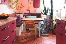 a maximalist kitchen with an orange wall, fuchsia cabinets, a mid-century modern chandelier and bold textiles