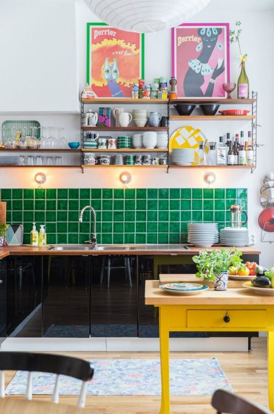 a maximalist kitchen with black sleek cabinets, an emerald tile backsplash, a yellow table, colorful artworks and open shelves