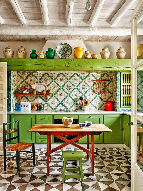 a maximalist kitchen with bold green cabinets and a wooden beam, bold printed tiles and geometric ones on the floor, a stained table and a woven chair