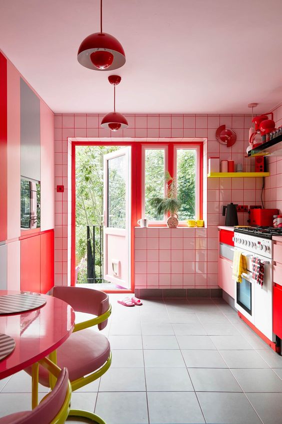 a maximalist kitchen with white tiles and red sprout, blush cabinets and red ones, neon yellow shelves and neon yellow and pink chairs